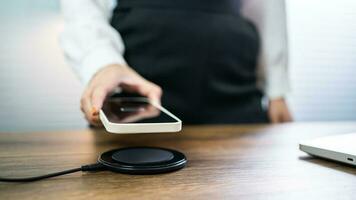 Charging mobile phone battery with wireless charging device in the table. Smartphone charging on a charging pad. Mobile phone near wireless charger Modern lifestyle technology concept. photo