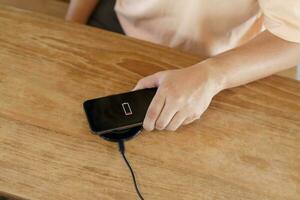 Charging mobile phone battery with wireless charging device in the table. Smartphone charging on a charging pad. Mobile phone near wireless charger Modern lifestyle technology concept. photo