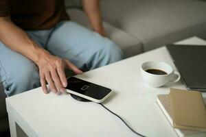 Charging mobile phone battery with wireless charging device in the table. Smartphone charging on a charging pad. Mobile phone near wireless charger Modern lifestyle technology concept. photo