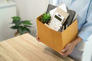 Business man sending resignation letter and packing Stuff Resign Depress or carrying business cardboard box by desk in office. Change of job or fired from company photo