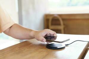 Charging mobile phone battery with wireless charging device in the table. Smartphone charging on a charging pad. Mobile phone near wireless charger Modern lifestyle technology concept. photo