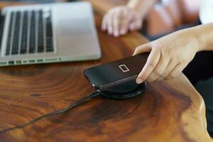 Charging mobile phone battery with wireless charging device in the table. Smartphone charging on a charging pad. Mobile phone near wireless charger Modern lifestyle technology concept photo