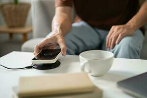 Charging mobile phone battery with wireless charging device in the table. Smartphone charging on a charging pad. Mobile phone near wireless charger Modern lifestyle technology concept. photo