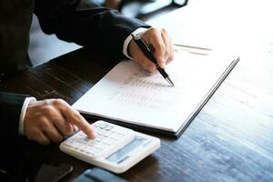 Businessman analyzing investment charts and pressing calculator buttons over documents. Accounting Concept. photo