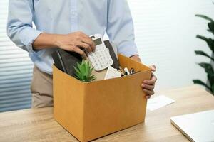 Business man sending resignation letter and packing Stuff Resign Depress or carrying business cardboard box by desk in office. Change of job or fired from company photo