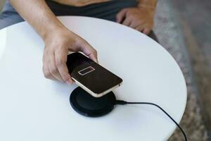 Charging mobile phone battery with wireless charging device in the table. Smartphone charging on a charging pad. Mobile phone near wireless charger Modern lifestyle technology concept. photo