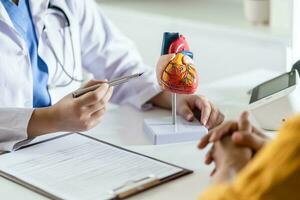 Cardiology Consultation treatment of heart disease. Doctor cardiologist while consultation showing anatomical model of human heart with aged patient talking about heart diseases. photo