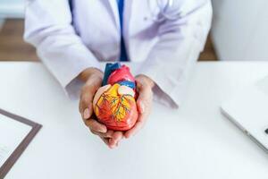 médico con anatómico modelo de humano corazón cardiólogo apoyos el corazón. corazón diagnosticar médico chequeo cardiólogo en examen habitación foto