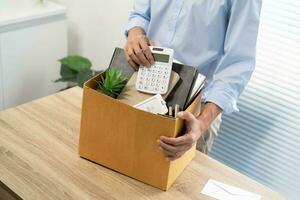 Business man sending resignation letter and packing Stuff Resign Depress or carrying business cardboard box by desk in office. Change of job or fired from company photo