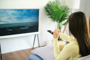 Asian woman Watching smart TV and using remote controller Hand holding television audio remote control at home with the remote control television photo