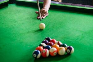 Man's hand and Cue arm playing snooker game or preparing aiming to shoot pool balls on a green billiard table. Colorful snooker balls on green frieze. photo