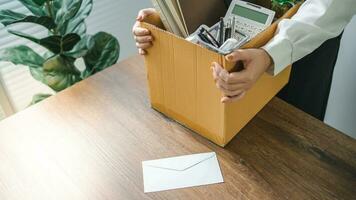 Business woman sending resignation letter and packing Stuff Resign Depress or carrying business cardboard box by desk in office. Change of job or fired from company photo