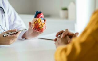 Cardiology Consultation treatment of heart disease. Doctor cardiologist while consultation showing anatomical model of human heart with aged patient talking about heart diseases. photo