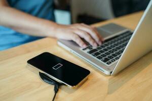 Charging mobile phone battery with wireless charging device in the table. Smartphone charging on a charging pad. Mobile phone near wireless charger Modern lifestyle technology concept photo