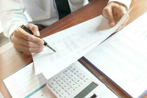 Businessman analyzing investment charts and pressing calculator buttons over documents. Accounting Concept. photo