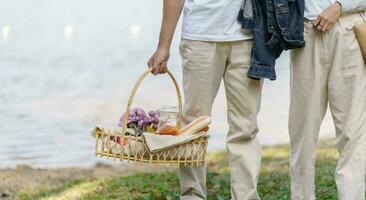 Pareja caminando en jardín con picnic cesta. en amor Pareja es disfrutando picnic hora en parque al aire libre foto