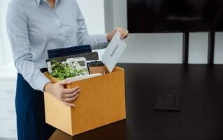 Business woman sending resignation letter and packing Stuff Resign Depress or carrying business cardboard box by desk in office. Change of job or fired from company. photo