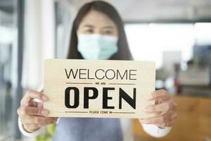 Young Asia girl wear face mask turning a sign from closed to open sign after lockdown. photo