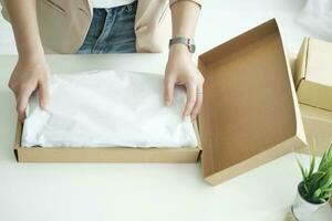 Asian female clothes shop owner folding a t-shirt and packing in a cardboard parcel box. photo