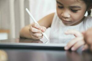 pequeño niña con tableta y aguja aprendizaje dibujo en línea foto