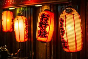 Red Japanese lanterns with inscriptions of Okonomiyaki which is a traditional food, on the door of a restaurant where it is cooked photo