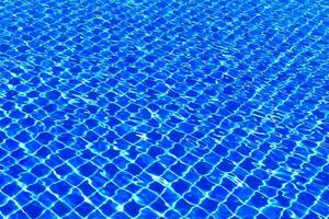 The blue tiles floor under the clear water in the swimming pool background, Swimming pool surface with floor mosaic tiles in blue photo