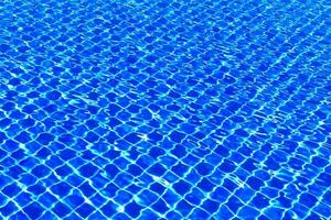 The blue tiles floor under the clear water in the swimming pool background, Swimming pool surface with floor mosaic tiles in blue photo