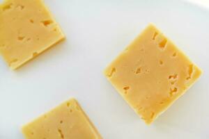 Yellow pieces of cheese on a white background. Square cheese. Delicious cheese snack. photo