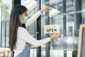 Young Asia girl wear face mask turning a sign from closed to open sign after lockdown. photo
