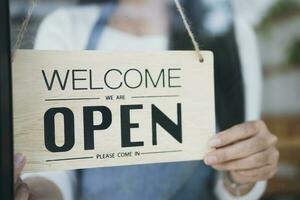 Close up of woman hands holding sign now we are open support local business. photo