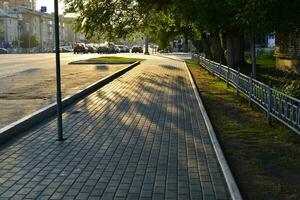 Summer city street in the setting sun. People walking away into the distance. City summer road and sidewalk. photo