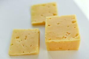 Yellow pieces of cheese on a white background. Square cheese. Delicious cheese snack. photo