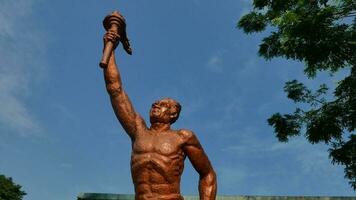 Surakarta, Indonesia, Vigésimo junio 2023, estatua de espíritu de deporte en un formar de hombre participación antorcha en contra azul cielo, Patung obor manahan situado a el manahan estadio surakarta foto