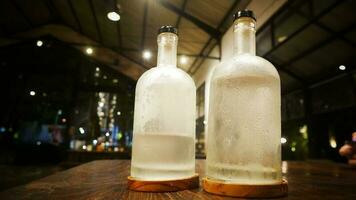 Selective focus, A clear glass bottle filled with cold water, clear glass bottle holds cold mineral water sits on wooden table, water use to quench thirst photo