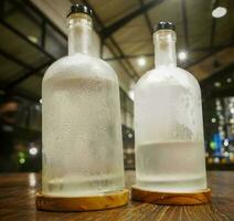 Selective focus, A clear glass bottle filled with cold water, clear glass bottle holds cold mineral water sits on wooden table, water use to quench thirst photo