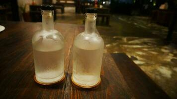 Selective focus, A clear glass bottle filled with cold water, clear glass bottle holds cold mineral water sits on wooden table, water use to quench thirst photo