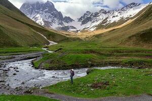 Trekker Taking Picture of View of Stream and Mountains While Trekking on Trail at Juta Georgia photo