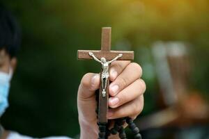 Wooden cross holding in hand with green and fresh forest background, concept for love of god in people around the world. photo