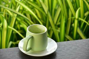 A cup of green tea on wooden table beside flower bed. photo