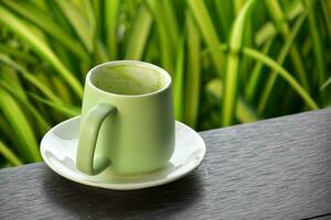 A cup of green tea on wooden table beside flower bed. photo