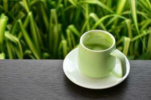A cup of green tea on wooden table beside flower bed. photo