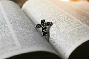 Closeup image of metal cross which places on opending bible book, soft focus, concept for religious lifestyle of christian people around the world. photo