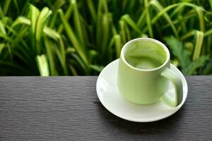 A cup of green tea on wooden table beside flower bed. photo