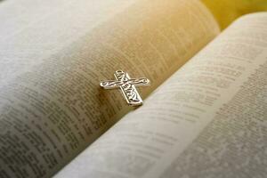 Closeup image of metal cross which places on opending bible book, soft focus, concept for religious lifestyle of christian people around the world. photo