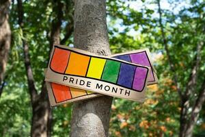 Signpost which has rainbow drawing with texts 'Happy Pride Month' sticked on tree trunk in public park to celebrate and to greet LGBT people events in pride month and to respect gender diversity. photo