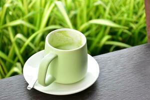 A cup of green tea on wooden table beside flower bed. photo