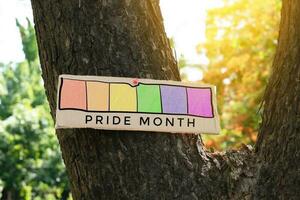 Signpost which has rainbow drawing with texts 'Happy Pride Month' sticked on tree trunk in public park to celebrate and to greet LGBT people events in pride month and to respect gender diversity. photo