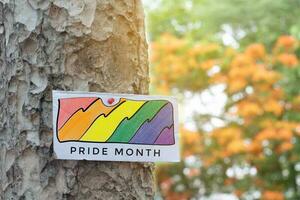 Signpost which has rainbow drawing with texts 'Happy Pride Month' sticked on tree trunk in public park to celebrate and to greet LGBT people events in pride month and to respect gender diversity. photo