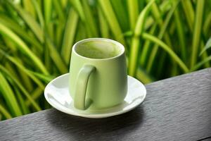 A cup of green tea on wooden table beside flower bed. photo