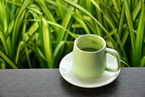 A cup of green tea on wooden table beside flower bed. photo